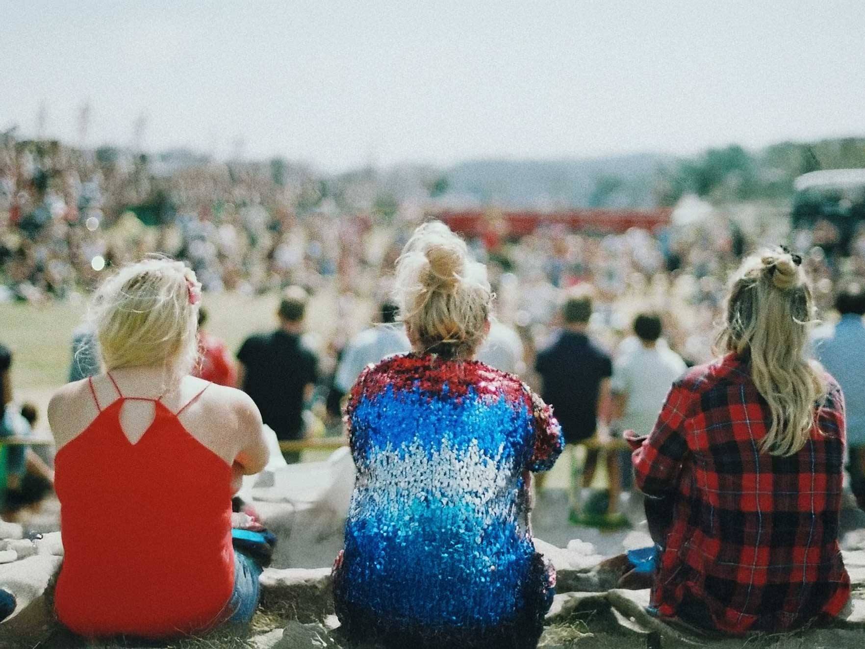 3 Junge frauen sitzen nebeneinander im freien und schauen auf einen festplatz